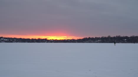 stunning winter sunset casts warm orange and yellow hues over a vast frozen lake in minnesota, creating a peaceful and serene landscape