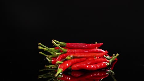 red chili peppers rotate on a reflective black surface, highlighting their vibrant color and texture under dramatic lighting