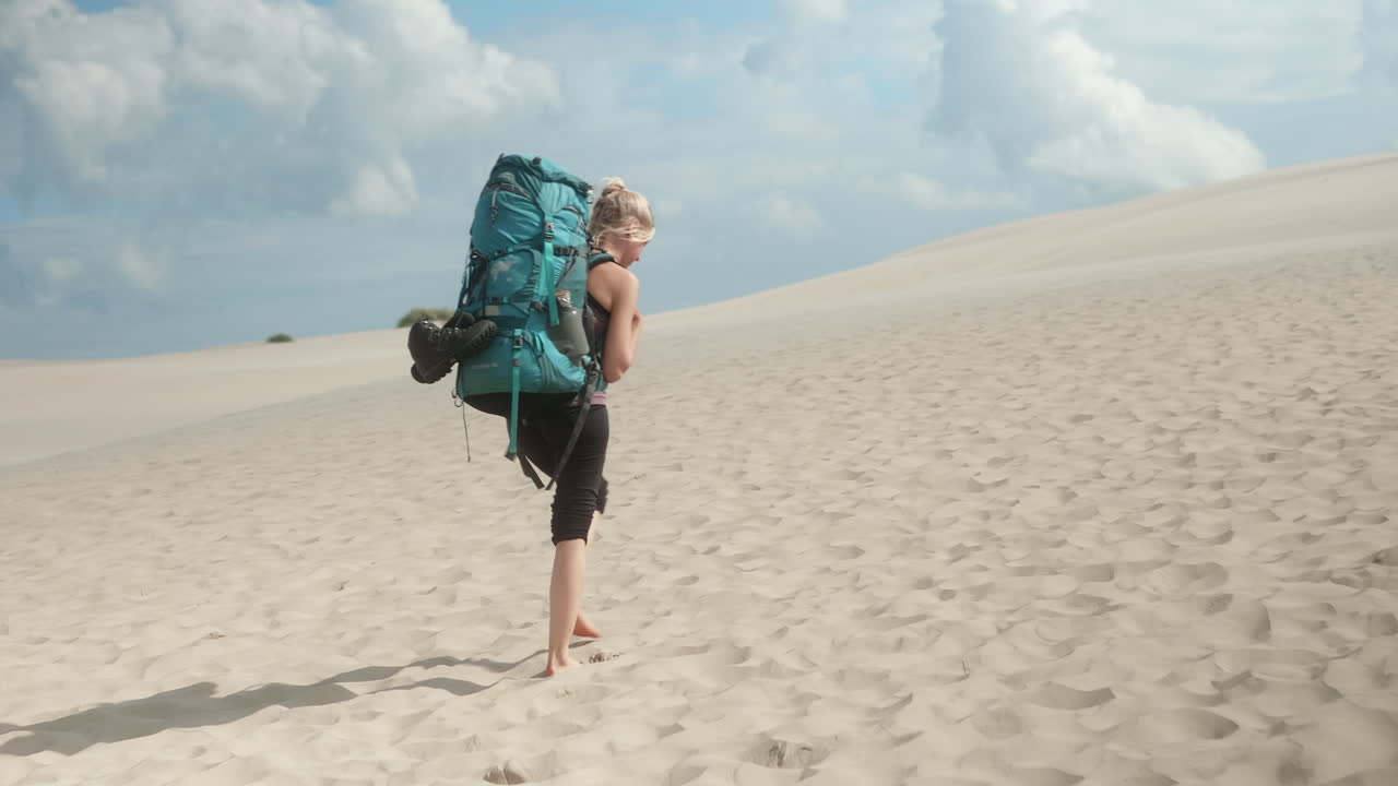 Blonde Female Hiker with Heavy Backpack Walking Up Barefoot a Sand Dune in the Desert on a Beautiful Summer Day, R&aring;bjerg Mile, Denmark