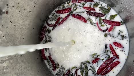 Pouring-Milk-Into-Large-Container-With-Herbs,-Spices,-And-Chili-Peppers