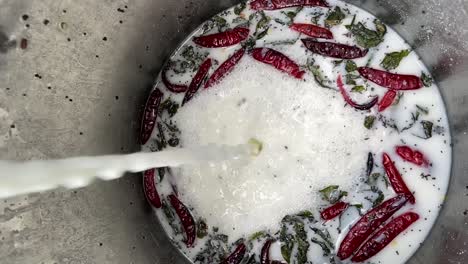 pouring milk into large container with herbs, spices, and chili peppers