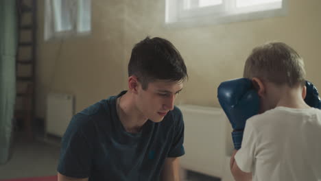 trainer works with kid in martial arts club. attentive combat instructor trains preschooler boy during boxing lesson in fighting gym slow motion