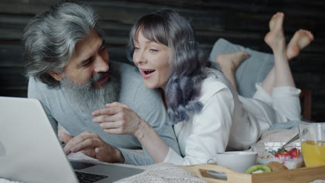 couple relaxing and using laptop in bed during breakfast