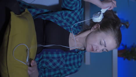 video vertical de una mujer triste e infeliz escuchando música por la noche en casa.