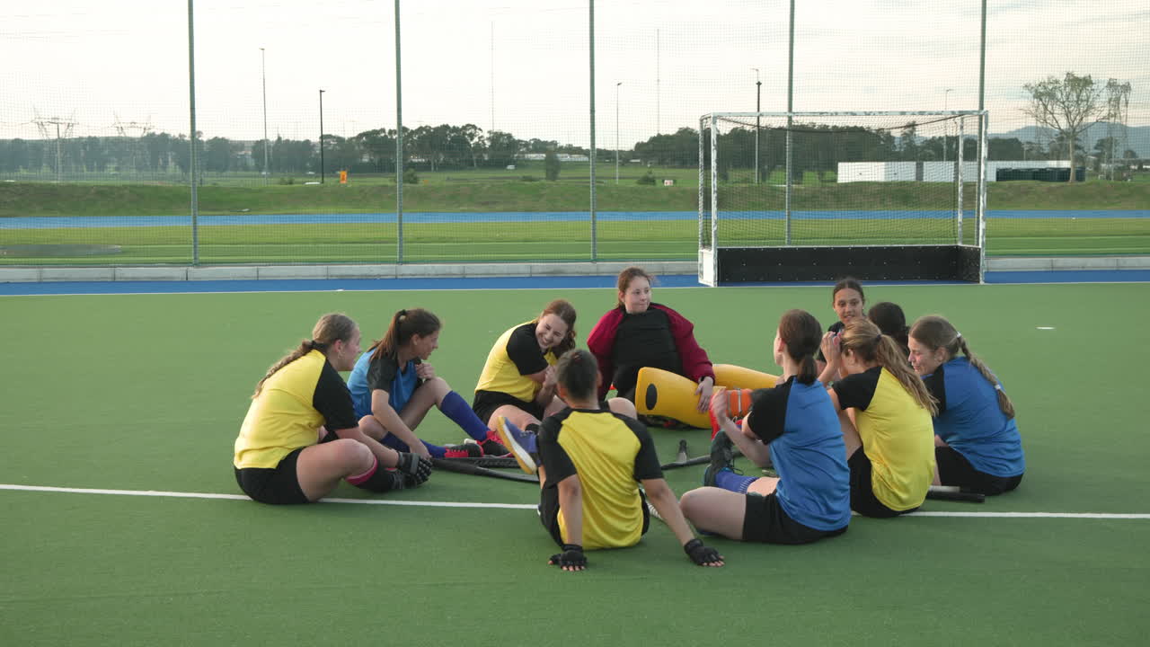 Female hockey team sitting on field, discussing strategy and bonding together