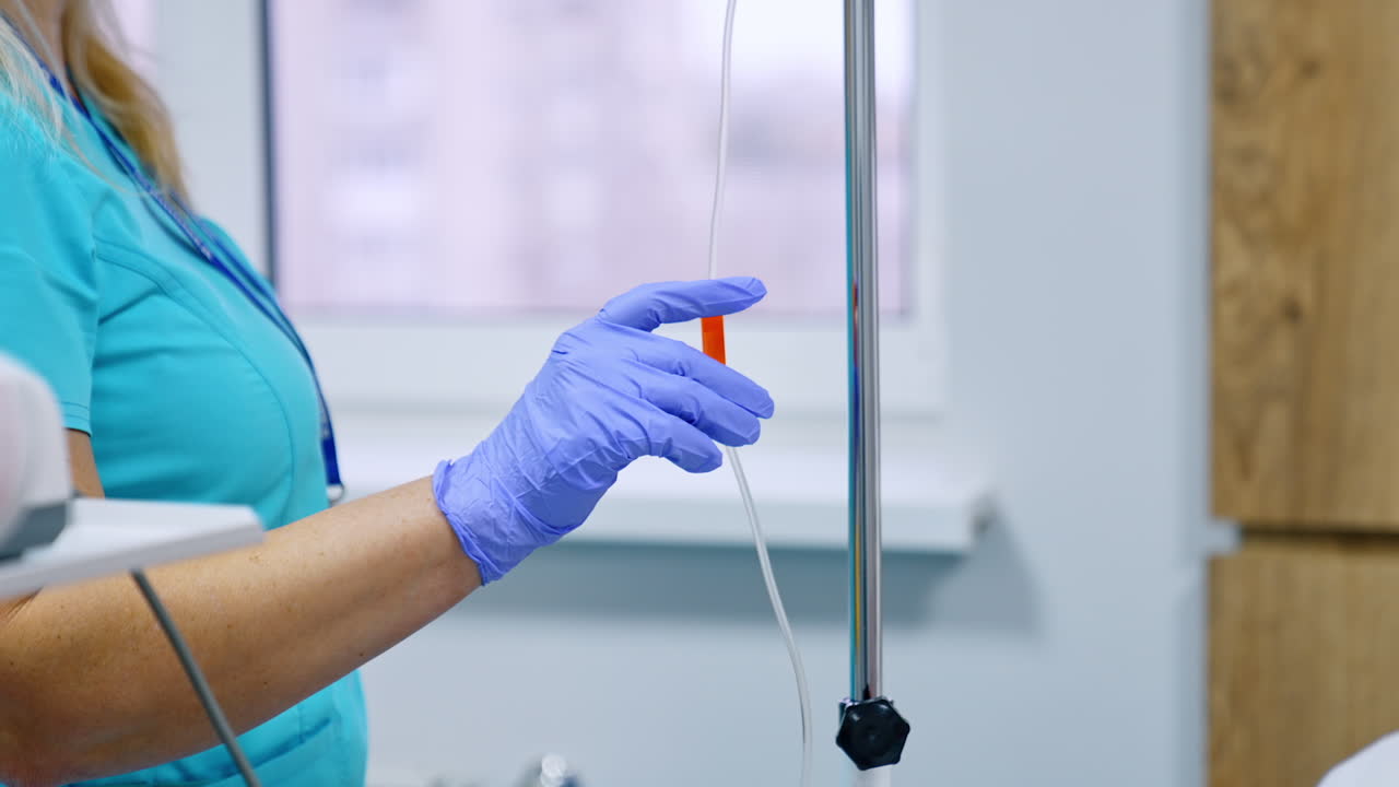 Unrecognized medical worker in blue latex gloves sets the drop counter. Nurse near the equipment in hospital ward.