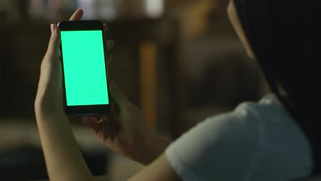 una adolescente sostiene un teléfono inteligente con pantalla verde en modo retrato por la noche. estilo de vida casual.