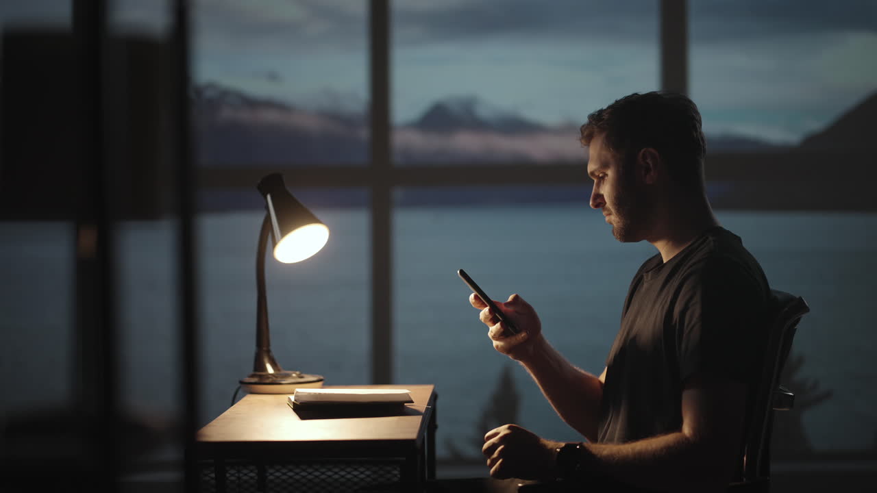 Silhouette of a man sitting at a table looking at a mobile phone thinking and analyzing the stock market solving personal problems repayment of loans Internet banking