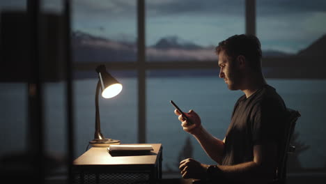 Silhouette-of-a-man-sitting-at-a-table-looking-at-a-mobile-phone-thinking-and-analyzing-the-stock-market-solving-personal-problems-repayment-of-loans-Internet-banking