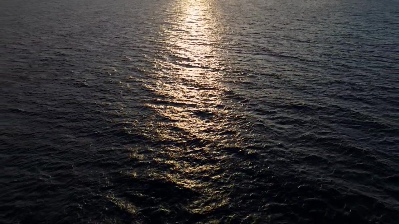 Aerial drone pullback of sunset reflection on the calm ocean surface, with golden light