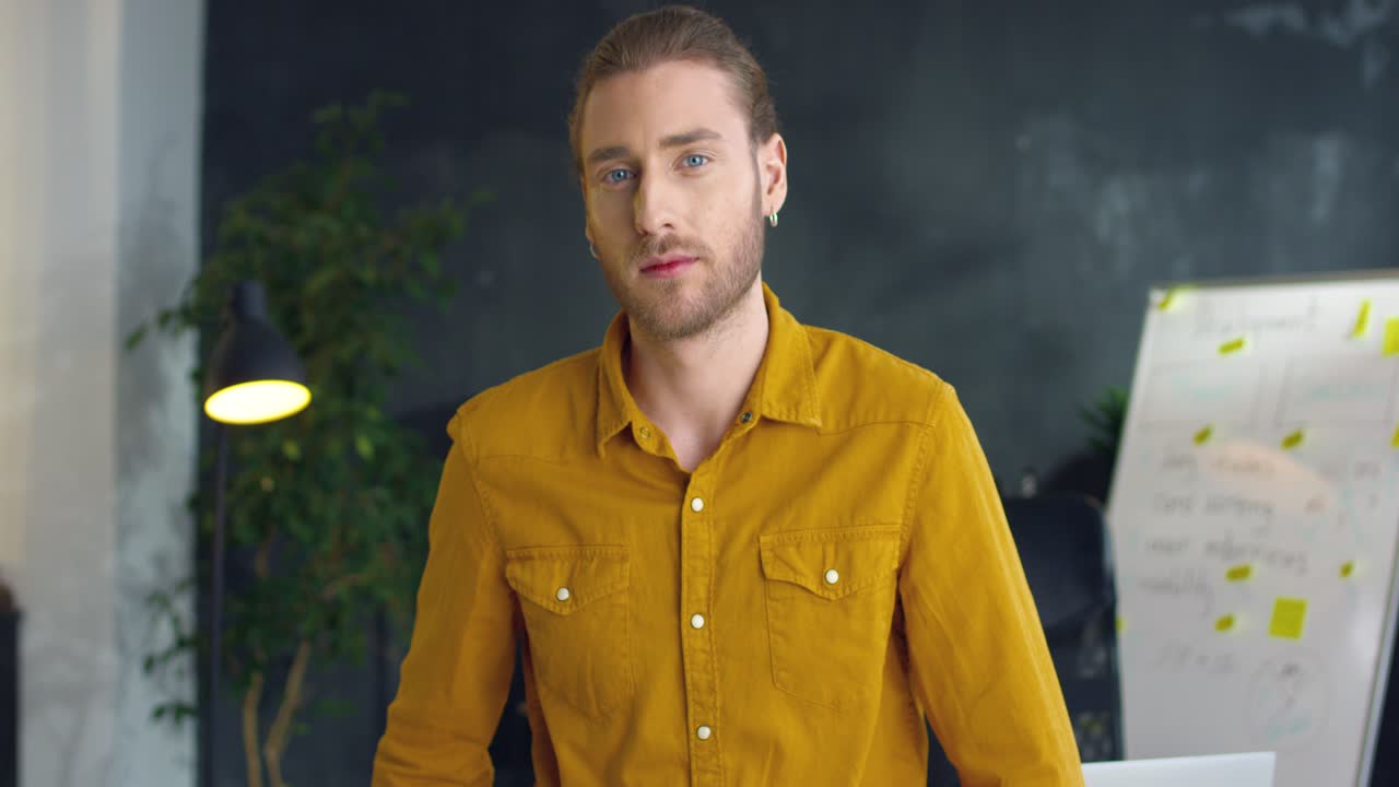 joven apuesto con camisa amarilla con las manos cruzadas sonriendo a la cámara en la oficina