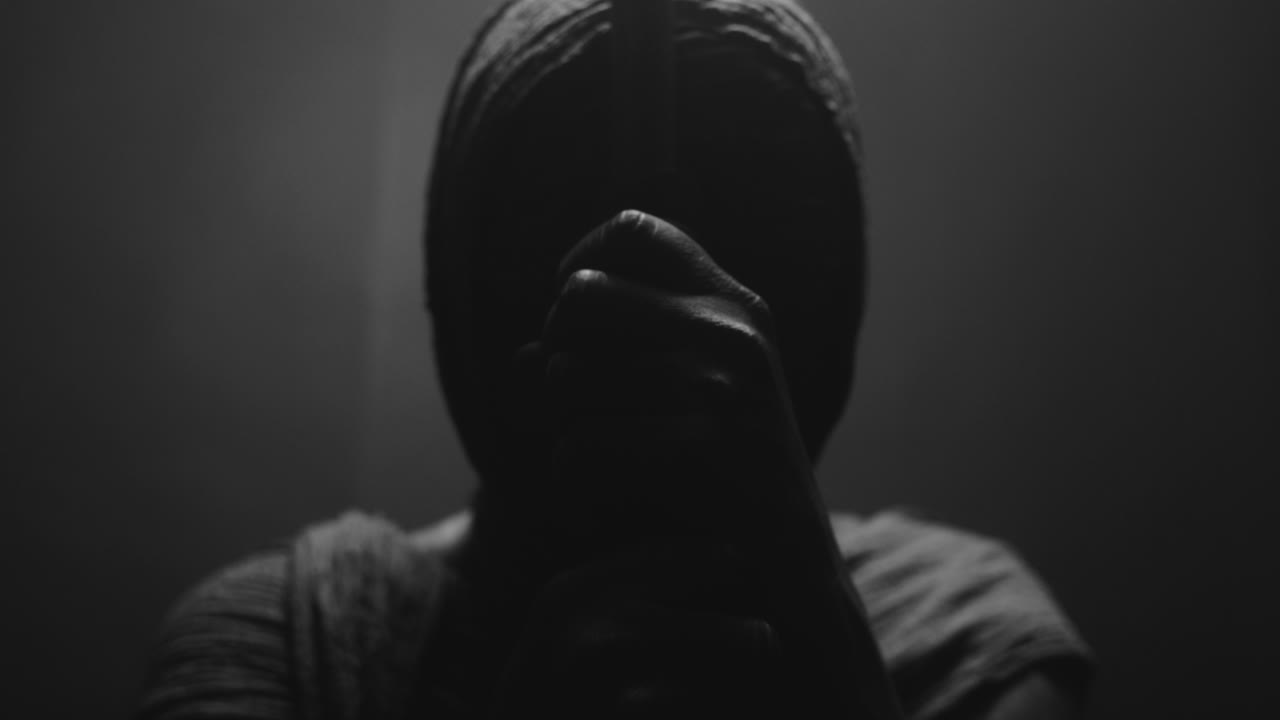 A mummified woman against the dark background pose with the walking staff