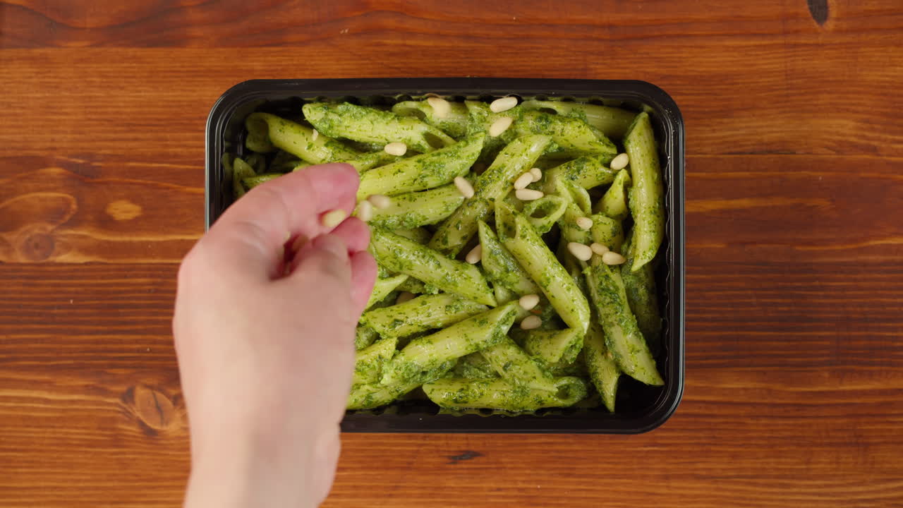 Hand Sprinkling Pine Nuts on Pesto Penne Pasta