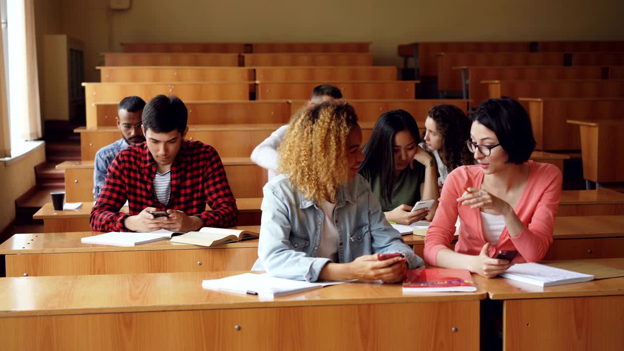 estudiantes alegres están usando teléfonos inteligentes y chateando durante el descanso entre las conferencias en la universidad. tecnología moderna, la juventud y el concepto de educación.