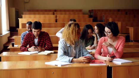 cheerful students are using smartphones and chatting during break between lectures at university. modern technology, youth and education concept.