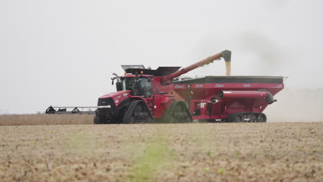 combine harvester transferring grain to bin pulled by tractor on a dusty farm field