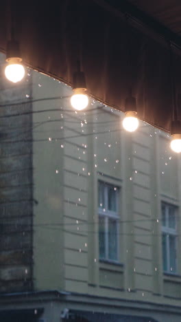 raindrops are falling on the roof of the restaurant with a decorative row of lamps on the background of building. it is raining. vertical video