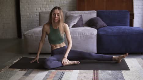 long haired young woman is doing stretching exercise sitting on mat in living room