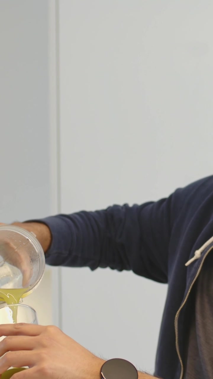 Video verticale: Uomo che solleva un barattolo e versa per riempire un bicchiere in cucina, con felpa con cappuccio e orologio, spazio per il testo.