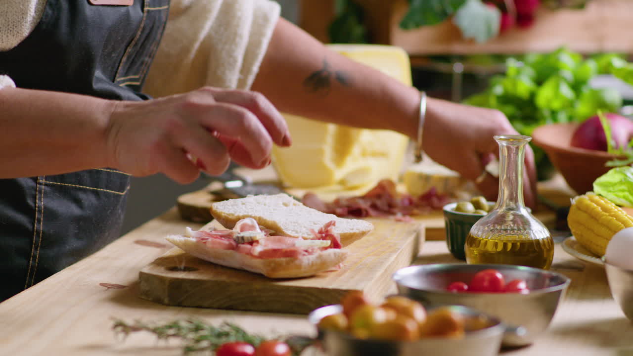 Preparing a sandwich with cheese, prosciutto, tomatoes and olives