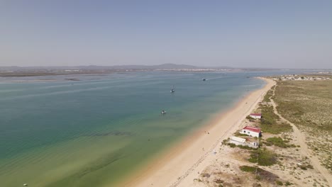 farol island beach with houses, clear blue water, and distant mountains in olhão, aerial view