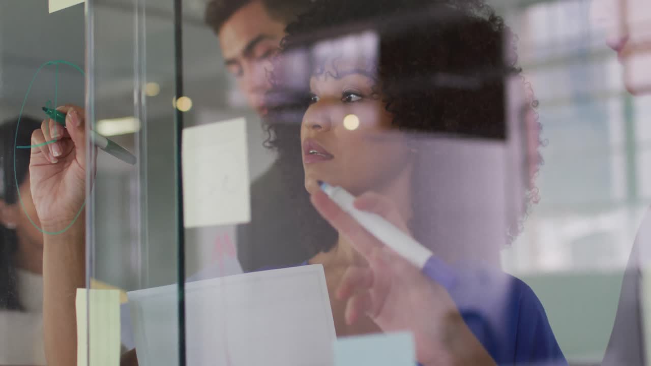 Diverse group of colleagues in meeting room brainstorming writing notes on glass wall