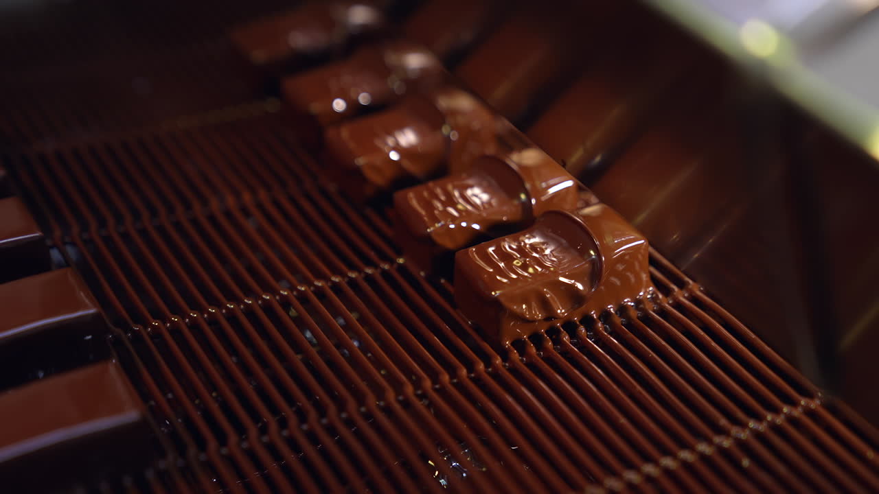 Bars of sweets covered with chocolate. Chocolate bars move along conveyor belt at confectionery factory for the production of sweets. Close up.