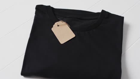 video of flat lay of black t shirt with tag and copy space on white background