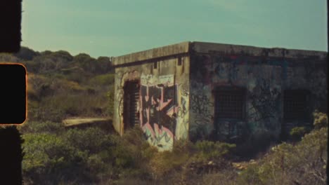 abandoned building covered in graffiti in an overgrown landscape