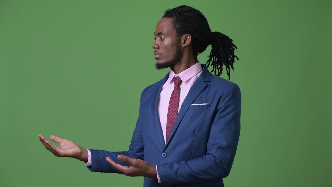 Young handsome African businessman with dreadlocks against green background