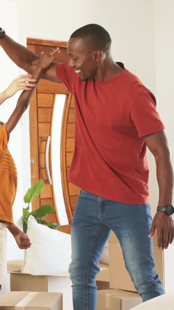 Father standing behind son, stepping back and lifting arm, cueing high five while unpacking boxes