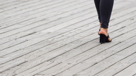 Close-up-of-a-woman's-feet-in-high-heels-on-a-wooden-boardwalk