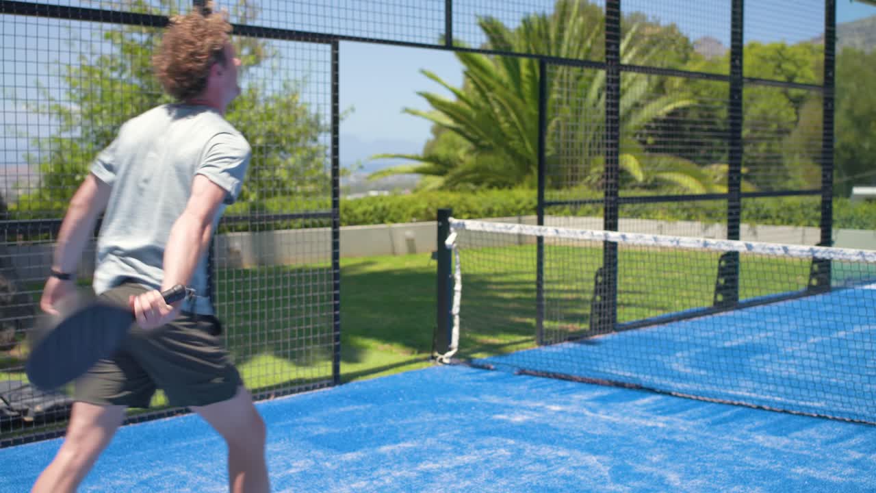 Männlicher Spieler wirft Ball zum Aufschlag auf blauem Spielfeld, schützt den Kopf und schüttelt dann Hände.