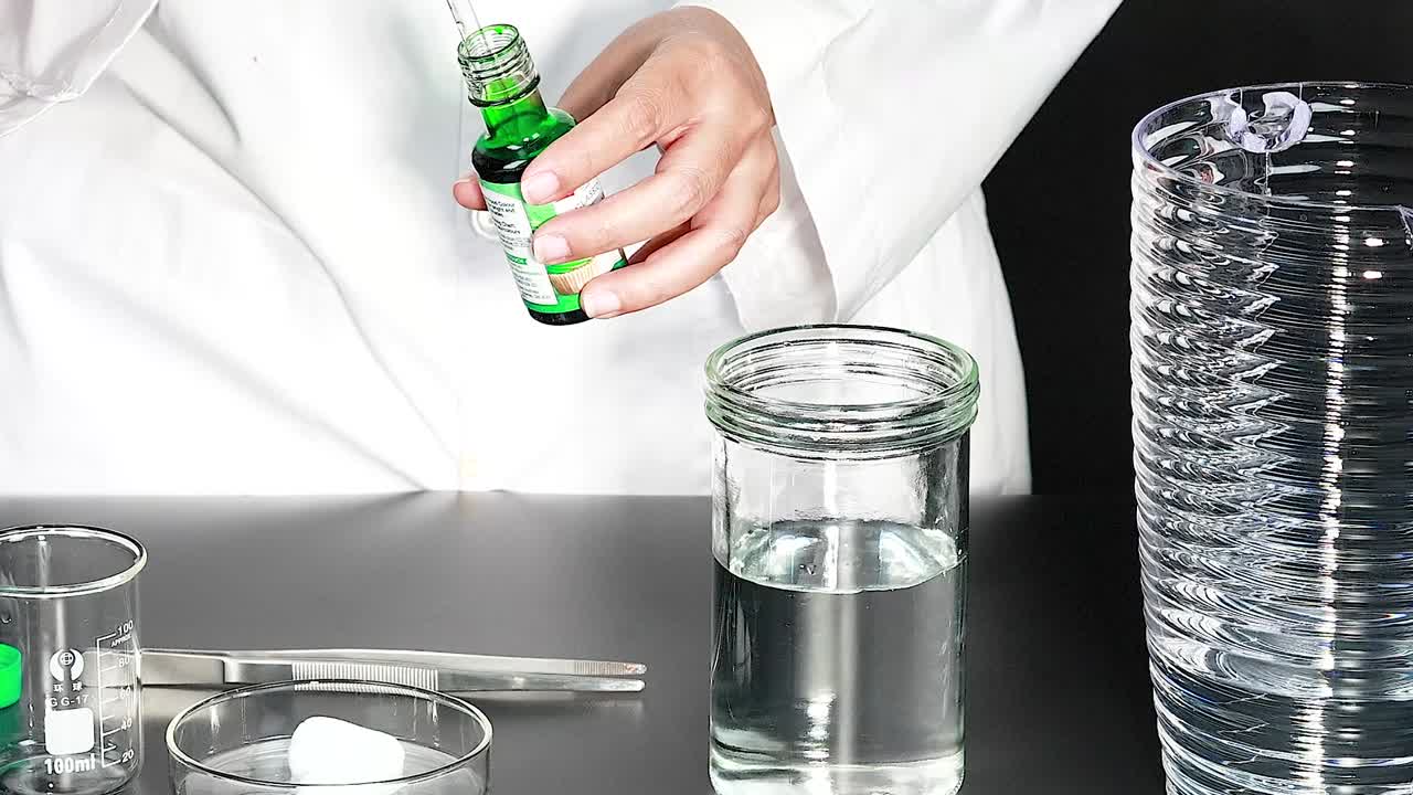 Eine Person im Laborkittel verwendet eine Pipette, um grüne Flüssigkeit in Glaswaren zu geben