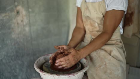 A-happy-young-potter-forms-a-piece-of-clay-on-a-special-potter's-wheel-in-his-studio.-The-concept-of-a-traditional-profession