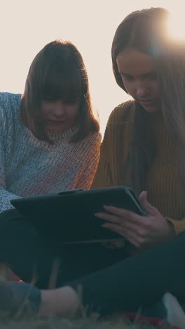 young long haired women with tablet and laptop work near tent at comfortable camp in autumn evening in bright sunset