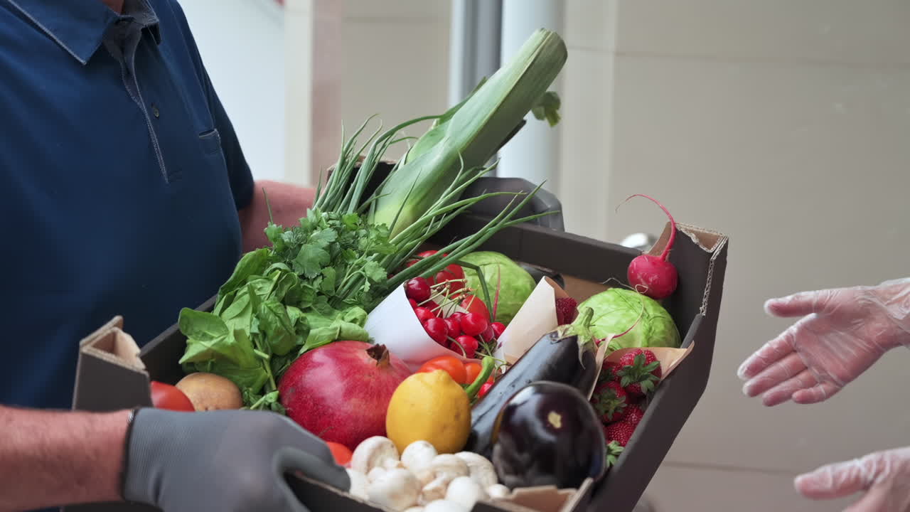 Woman receiving a box of fresh fruits and vegetables from a masked delivery man