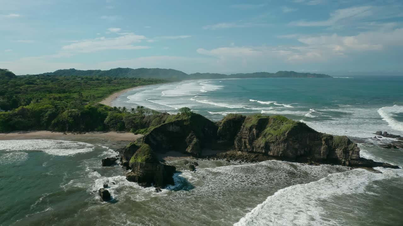 Vista aerea con drone di un promontorio roccioso a Guiones Beach a Nosara, Costa Rica, con onde che si infrangono lungo la costa.