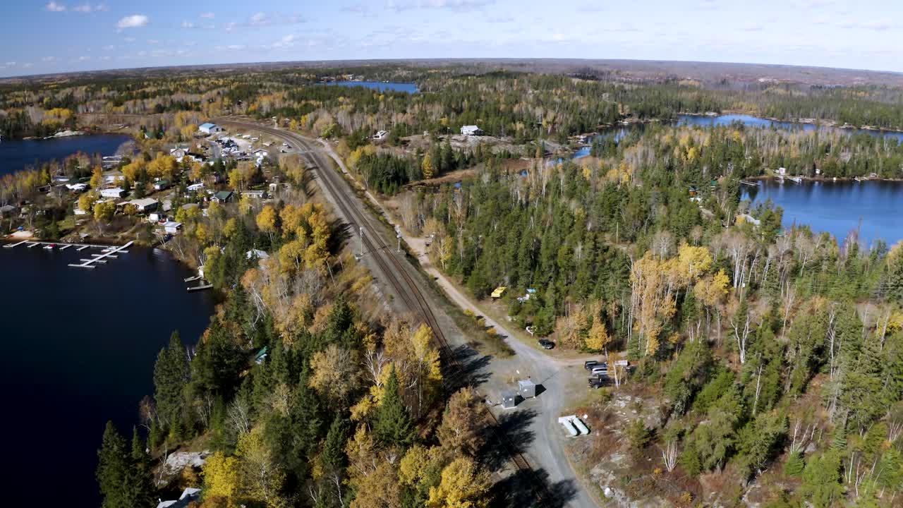 descenso aéreo del ferrocarril dividido escondido entre dos lagos con cabañas entre el bosque boreal de colores en el hermoso escudo canadiense idílico