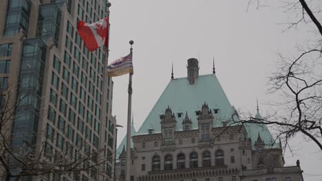 close up of canada and british columbia flags waving in front of fairmont hotel copper rooftop in downtown vancouver