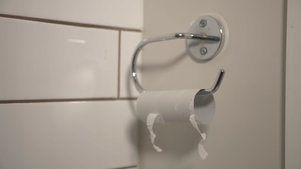 A Person Pulling The Last Pieces of A Toilet Paper On The Bathroom Wall - Closeup Shot