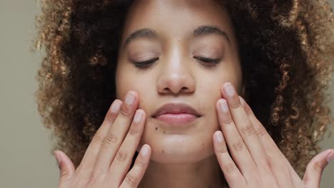 mujer biracial con cabello oscuro tocando la cara sobre un fondo beige, cámara lenta