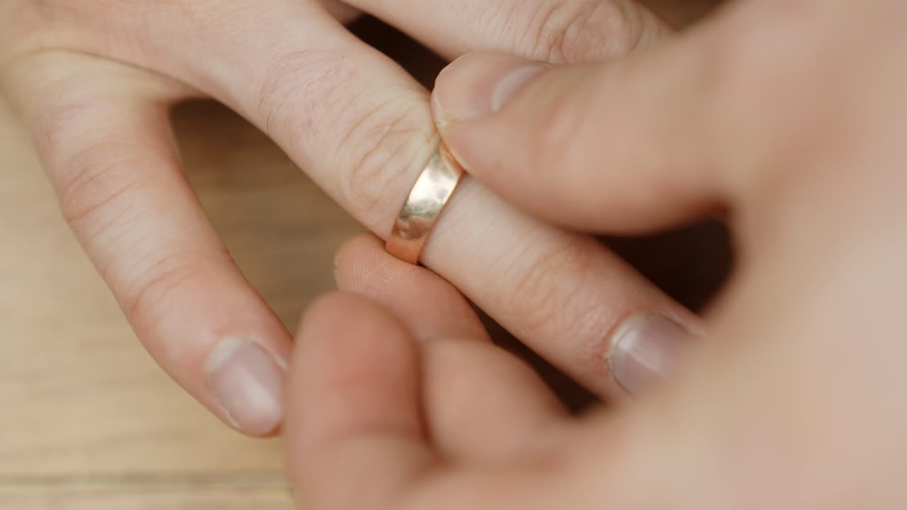 A close-up of a hand delicately placing a golden ring on the right ring finger, capturing a meaningful and intimate moment.
