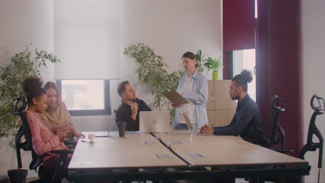 pregnant woman is explaining a project talking with a coworker in a meeting room while she is touching her belly 2