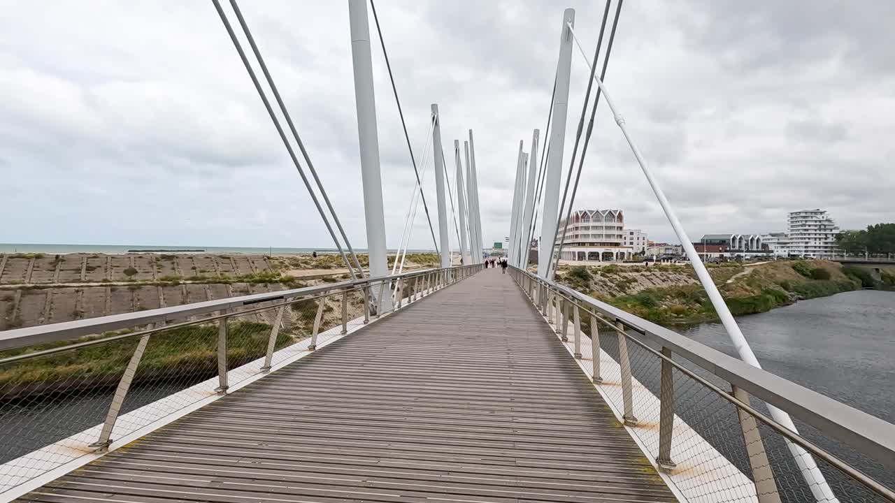 Steady camera glides along modern pedestrian bridge with metal supports in urban Dunkirk, France