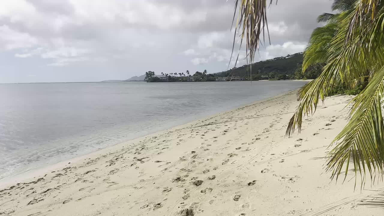 una tranquila playa en oahu, hawai, con huellas en la arena que conducen a lo largo de la costa