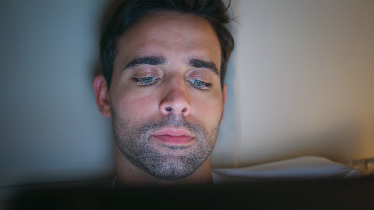 Closeup man looking tablet in bedroom capturing concentrated reading at night