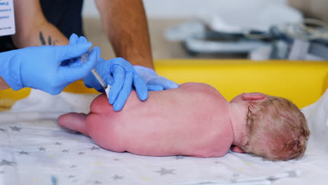 little newborn lies on its side back to the camera. doctor's hands in gloves give a shot to a baby's buttock.