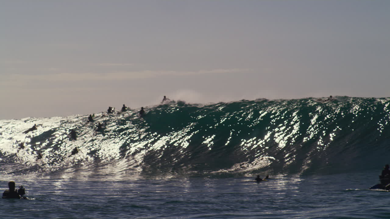 Panoraamanäkymä surffaajista jonossa yrittämässä napata jättimäistä aaltoa.