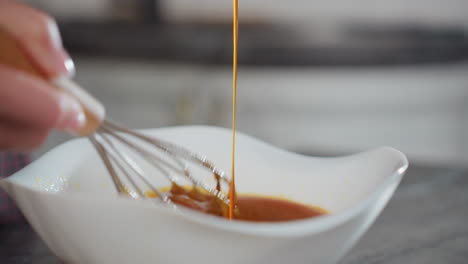 primer plano de una persona vertiendo una rica sopa roja en un cuenco blanco mientras se agita con un batidor, el líquido vibrante fluye suavemente a medida que los ingredientes se mezclan, creando una mezcla sabrosa en una cocina moderna